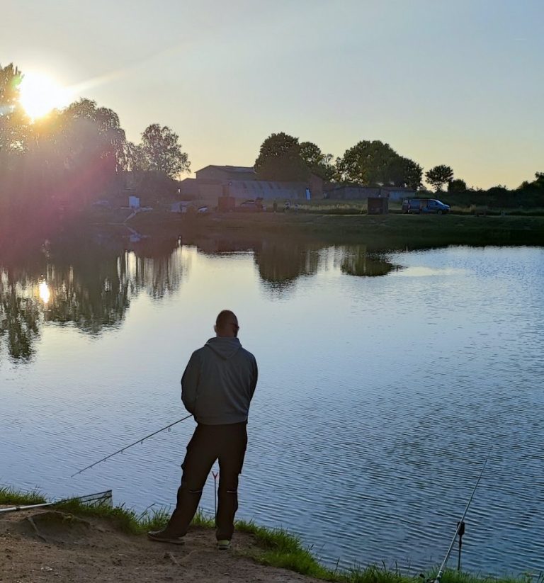 Angler steht am Ufer eines Gewässers und fischt bei Sonnenuntergang.